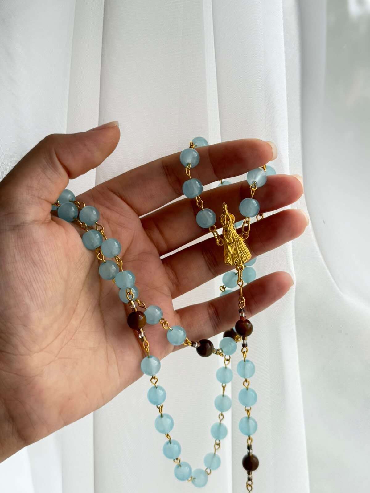 Soft clouded blue beads on warm-toned wire links laid open across a palm, with two darker brown notes low in the run and a small warm-toned standing figure at the centre